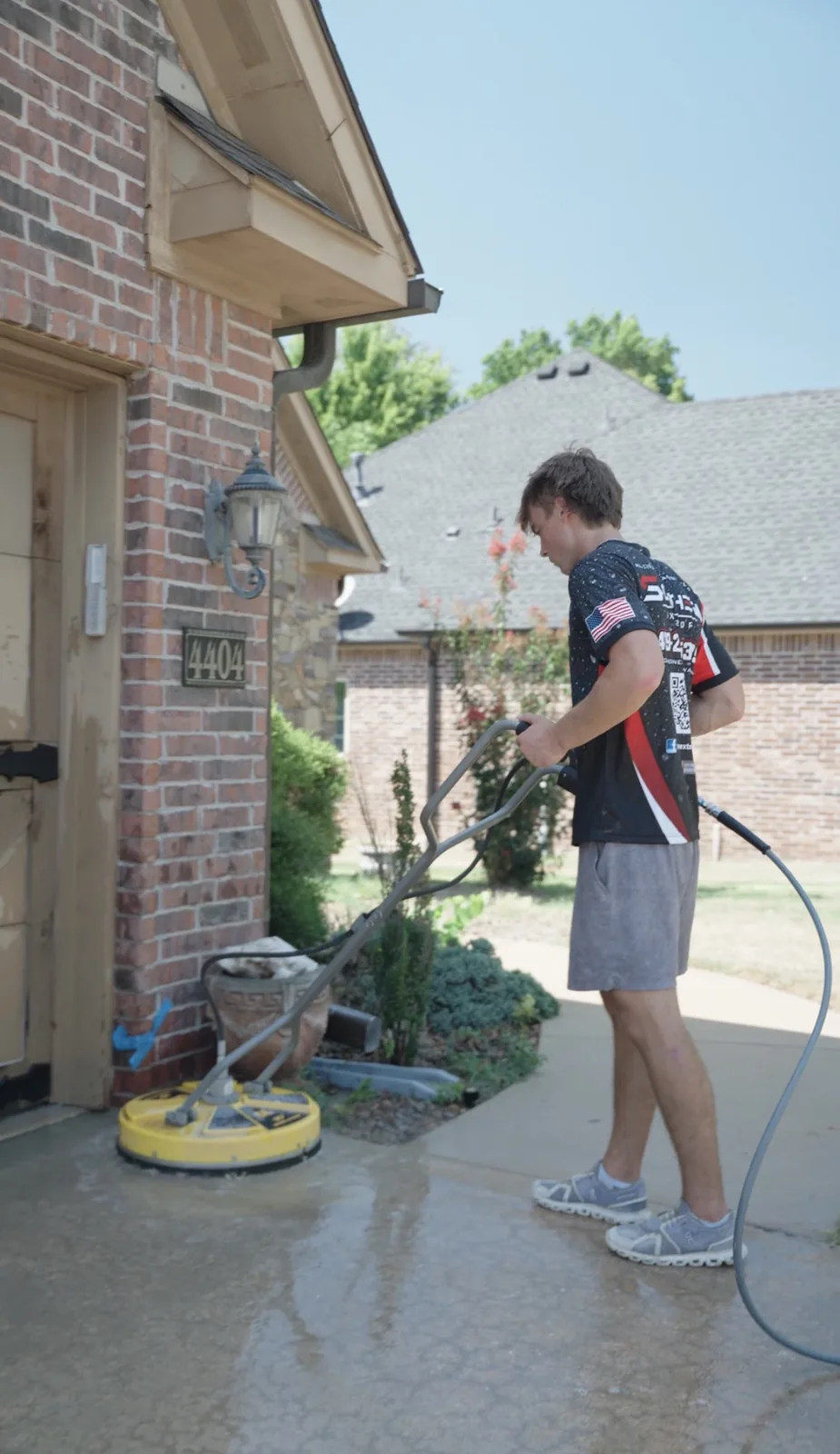 Southern Exterior technician running a surface cleaner across a concrete driveway at a Northwest Arkansas home